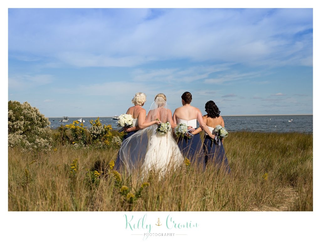 A bride and her bridal party walk in a field | Kelly Cronin Photography | Cape Cod Wedding Photographer