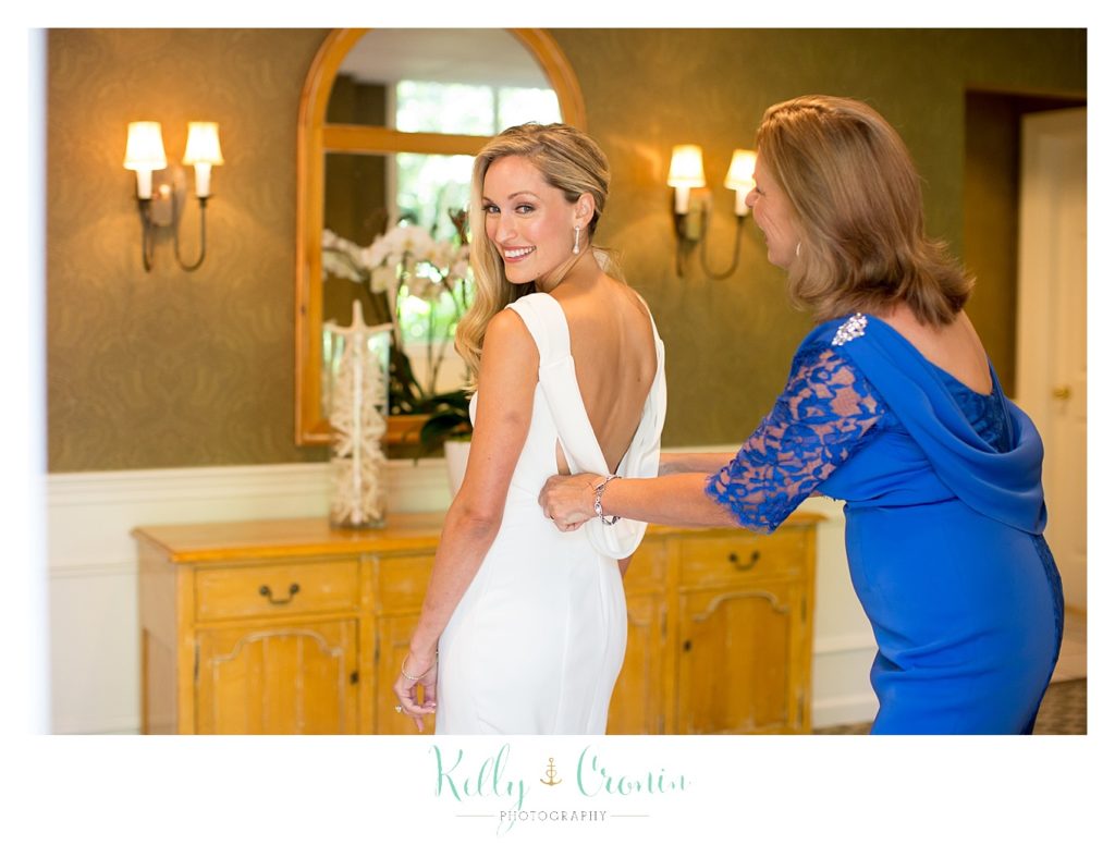 A mother zips her daughter's wedding dress, getting ready for a beautiful Romance in Cape Cod. | Captured by Kelly Cronin Photography