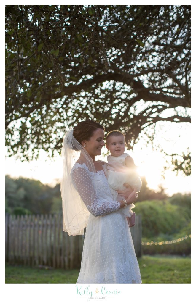 A bride holds the flower girl, this was a Mooncussers Tavern Reception, captured by Kelly Cronin Photography