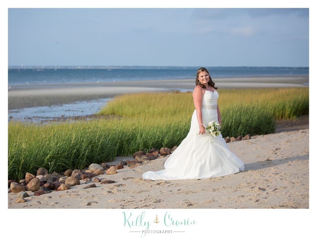A bride stands in front of a beautiful shoreline with many colors | Kelly Cronin Photography | Ocean Edge Resort and Golf Club