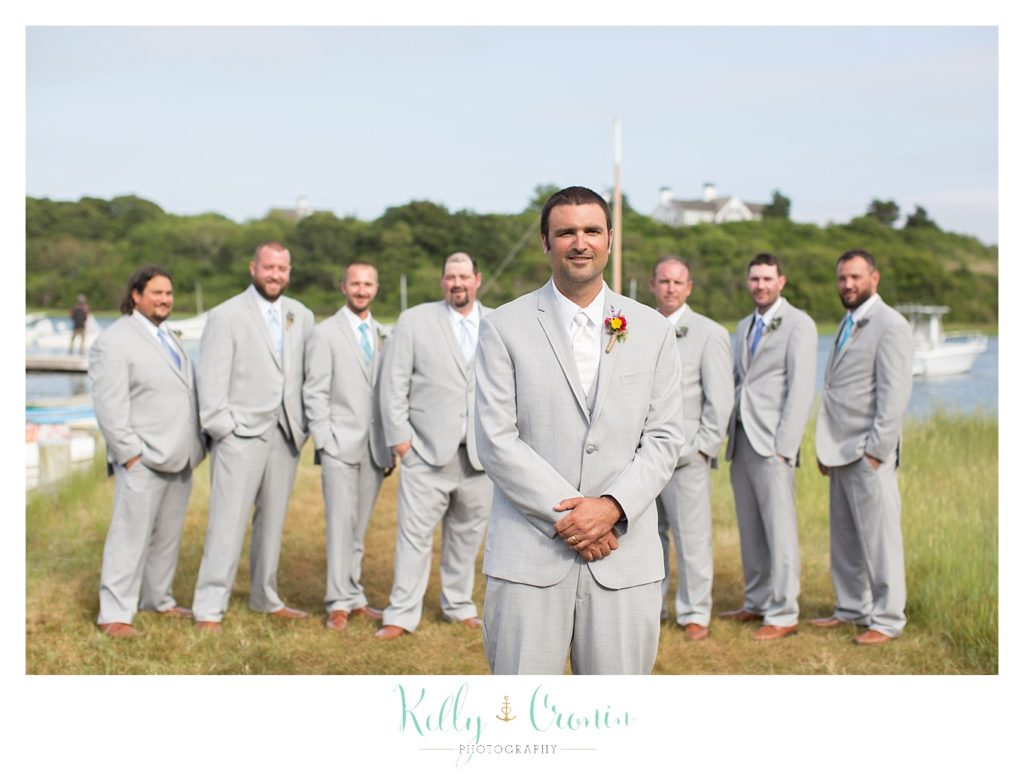 A groom stands in front of his groomsmen  | Kelly Cronin Photography | Oyster River Landing