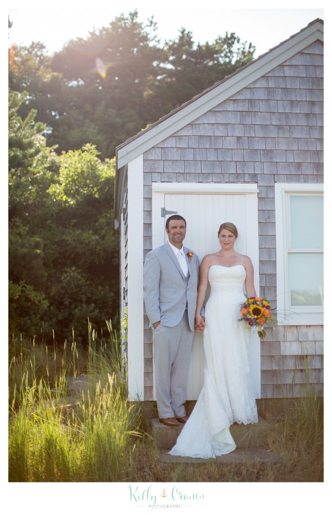 A newlywed couple stand in front of a cute building  | Kelly Cronin Photography | Oyster River Landing