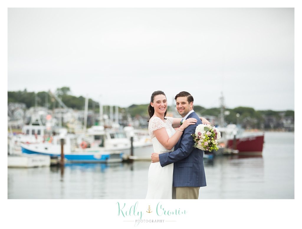 A bride and groom pose in front of boats | Kelly Cronin Photography | Pilgrim Monument