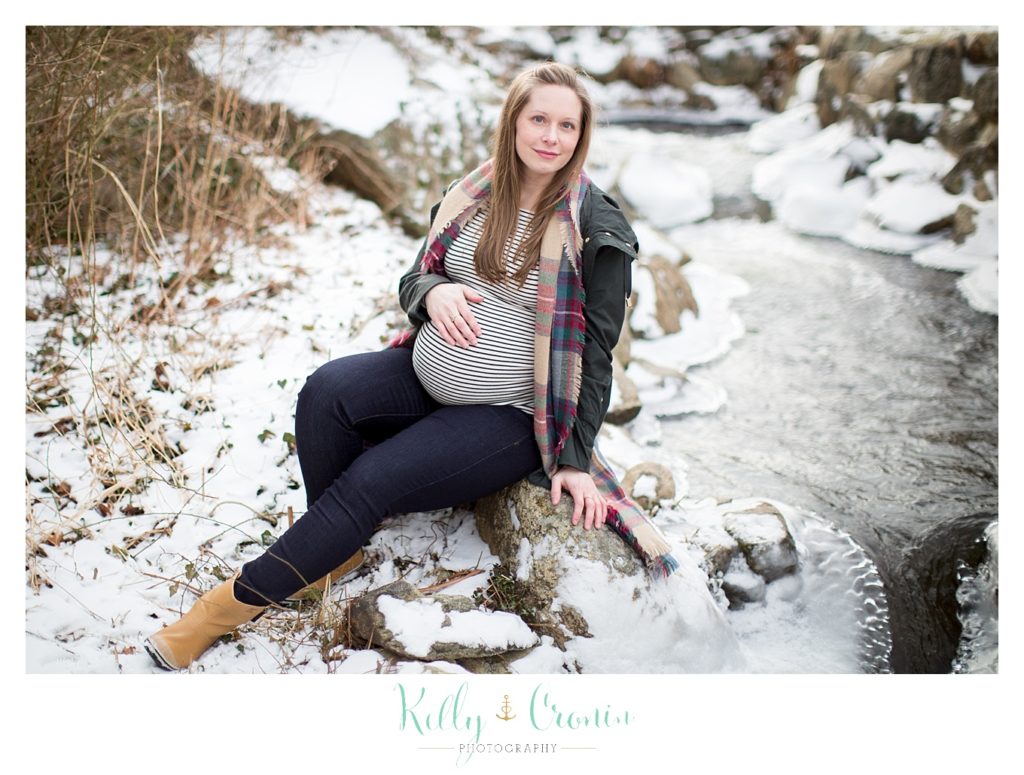 A pregnant woman sits in the snow  | Kelly Cronin Photography | Cape Cod Maternity Photographer