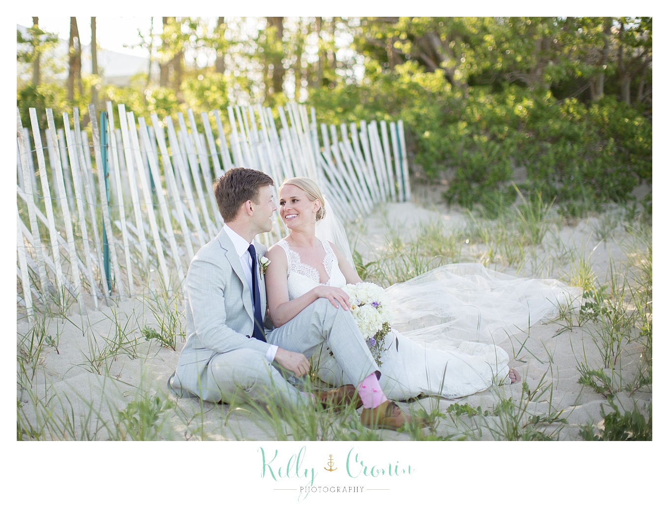 A bride and groom sit on the beach together.