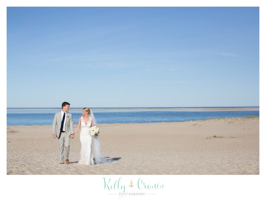 A couple take a walk on the beach on their wedding day. 