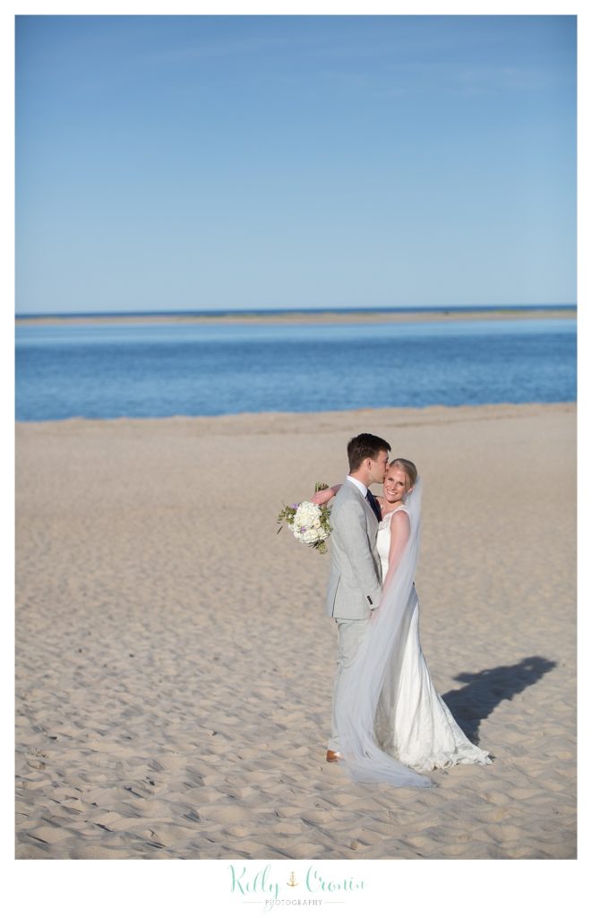 A man kisses his bride on the beach. 