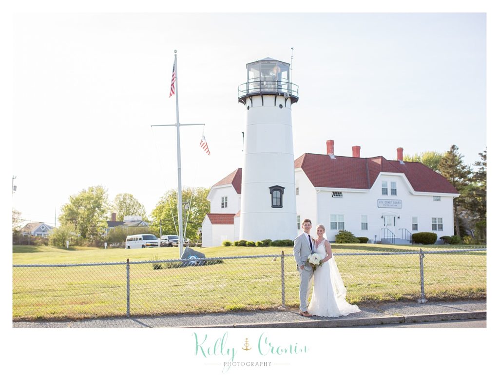 A bride and groom stand in front of a lighthouse. 