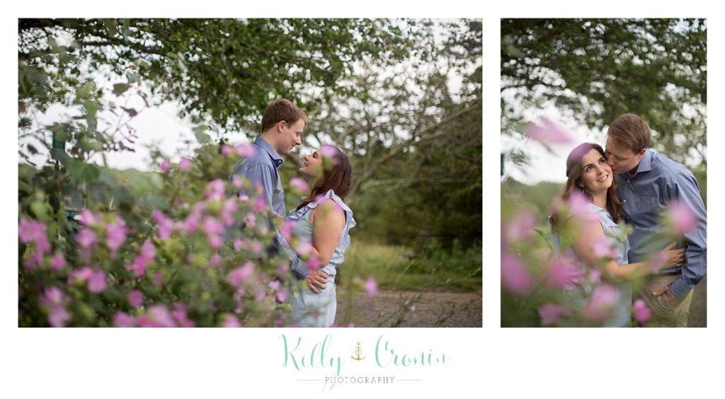 A man kisses his fiance behind some flowers in Thompson's Field. 