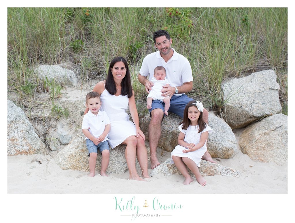 A family sits on rocks by the shore  | Kelly Cronin Photography | Seaside Session in Cape Cod