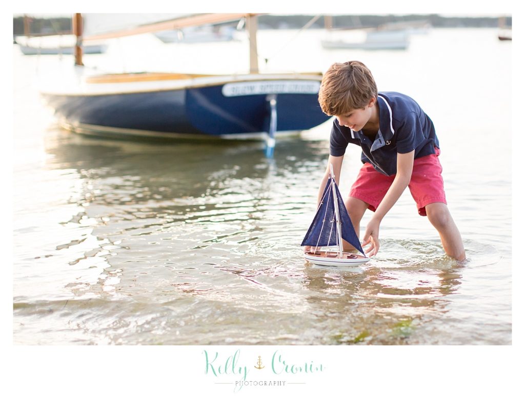 A boy plays with a toy sail boat. 