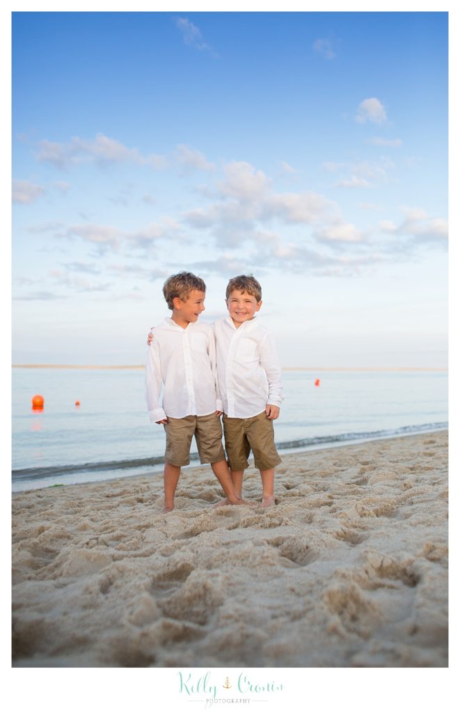 Two boys stand on the beach. 