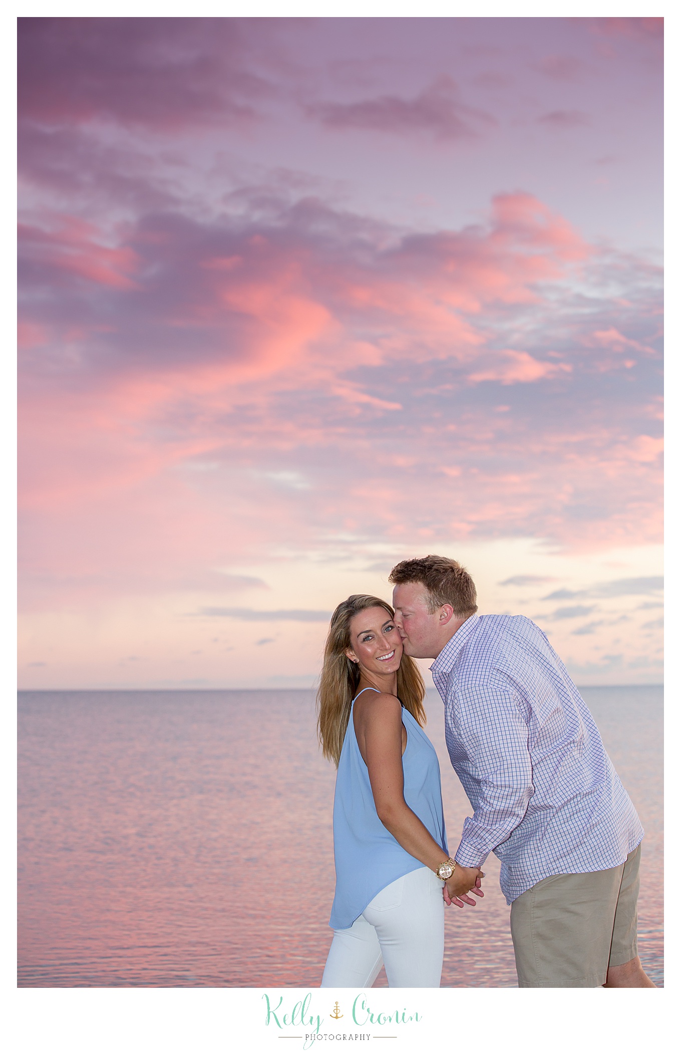 A man kisses his fiance in front of a sunset.