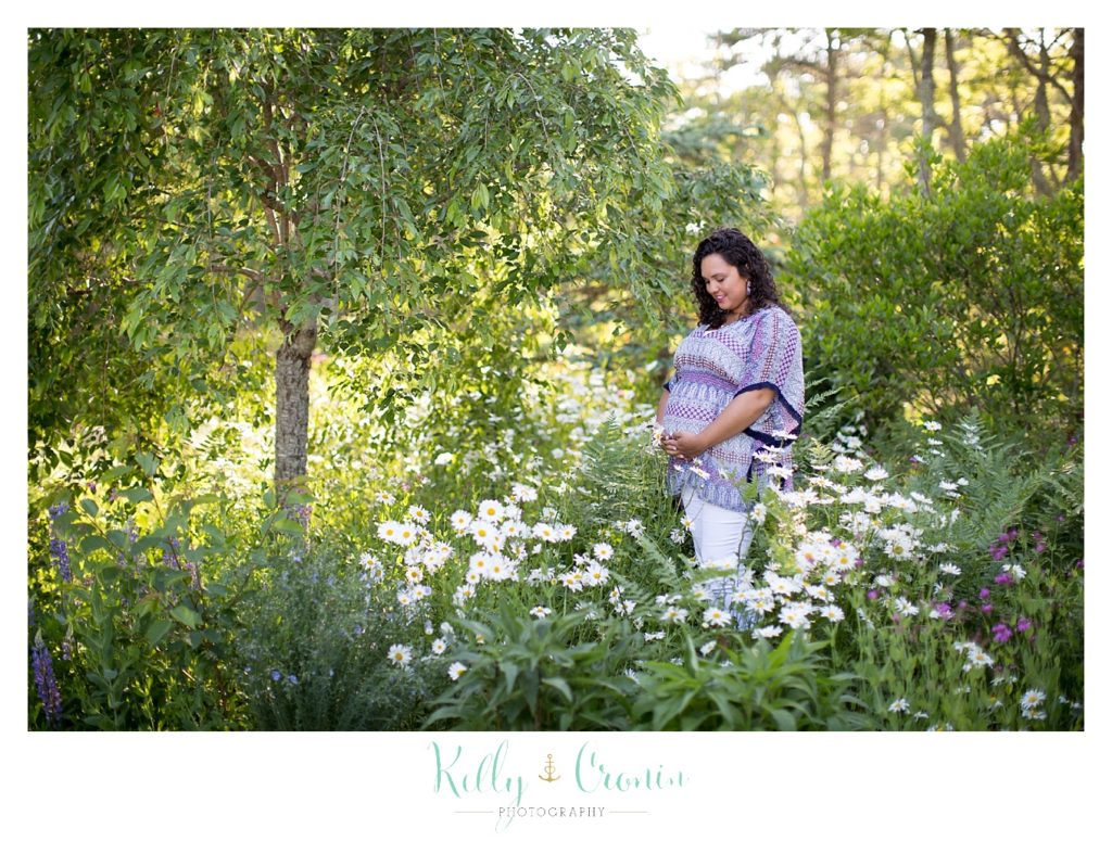 A pregnant woman stands in a field of flowers. 