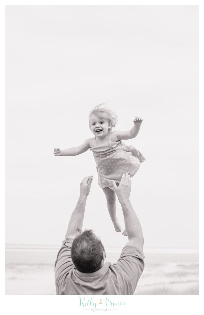 A father throws his daughter up in the air. 