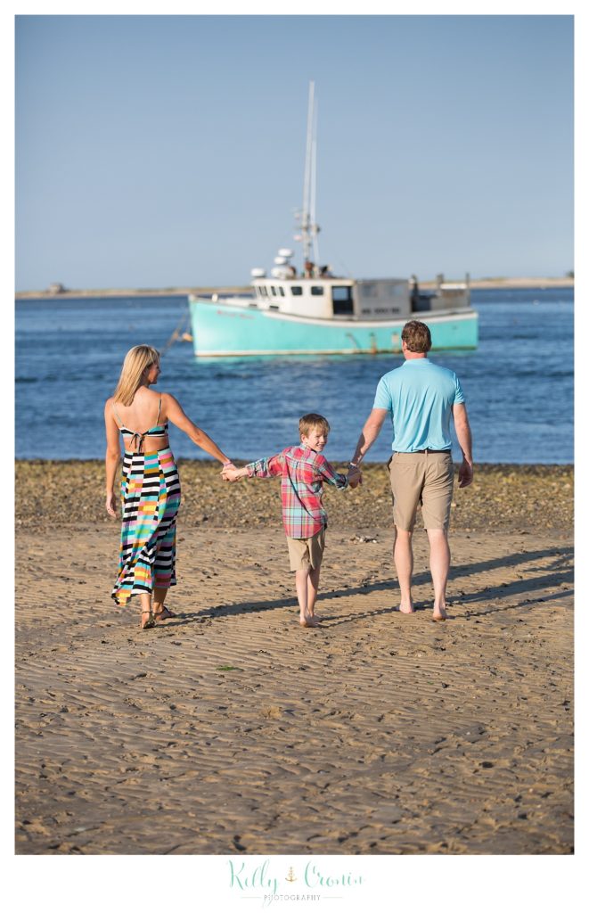 A family of three is taking a walk on the beach.