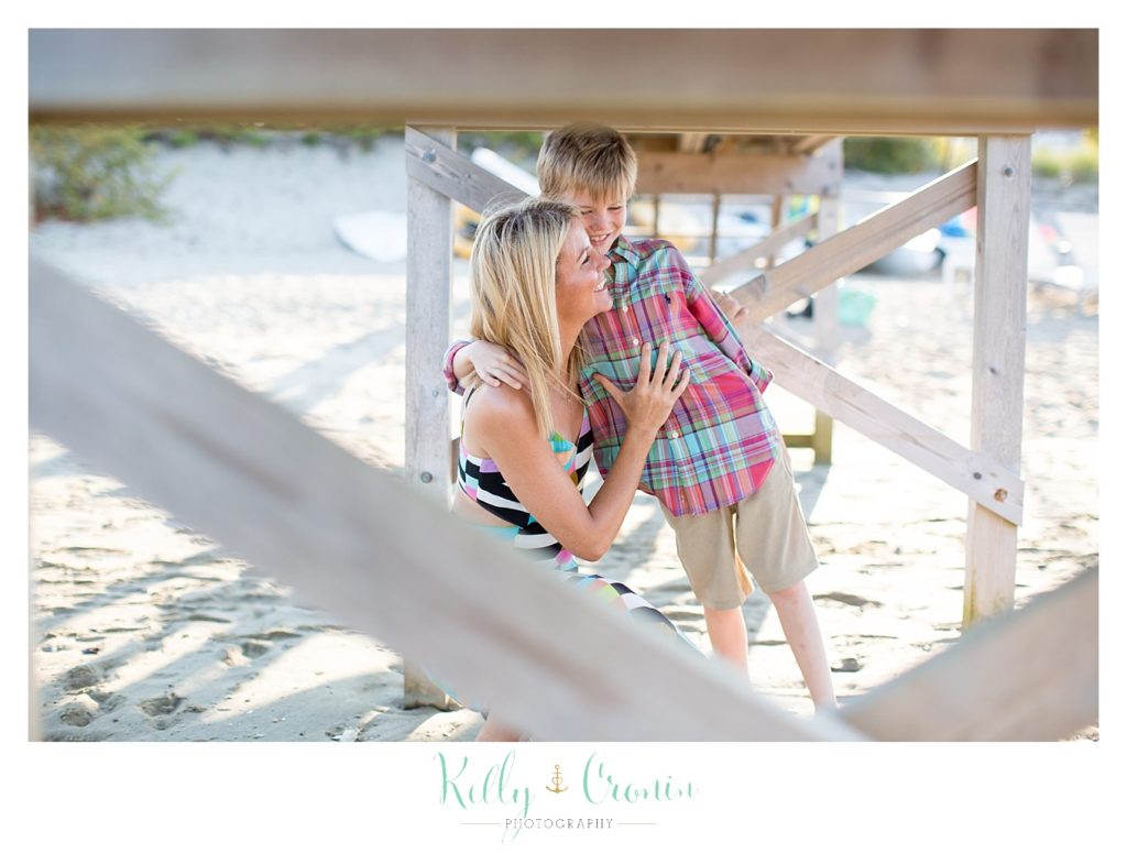 A mother pulls her son close under a bridge on the beach. 