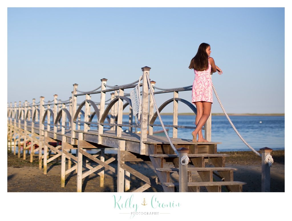 A girl stands on a pier, looking out into the ocean. 
