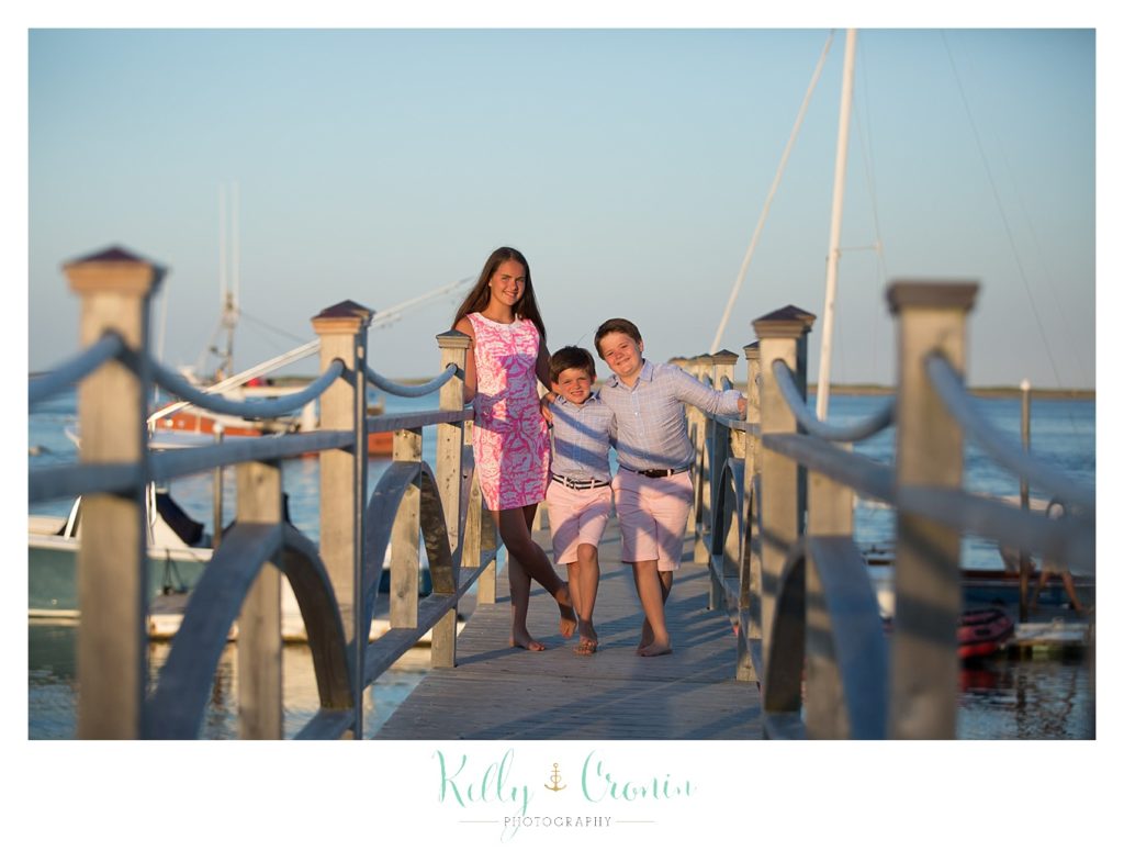 Three siblings stand on a pier together. 
