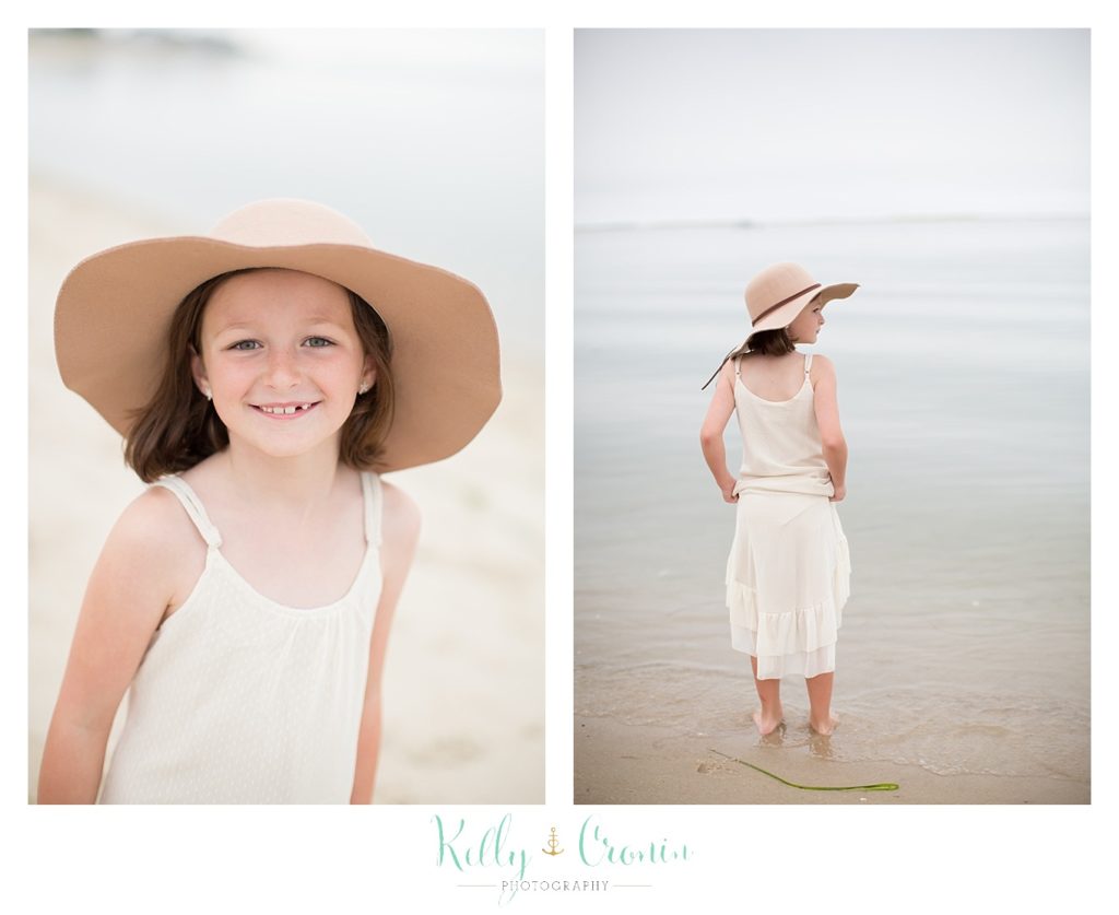 A little girl wears a big straw hat on the beach. 