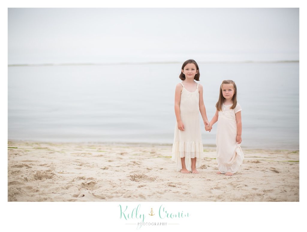 Sisters hold hands while standing on a beach | Family Photographer In The Cape