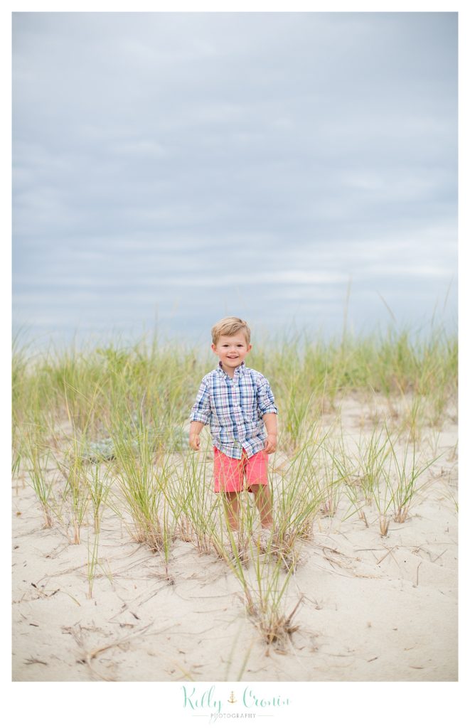 A boy stands in the grass on a beach in Cape Cod. 