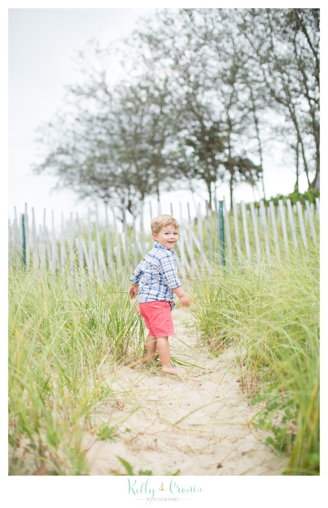 A little boy takes a walk down a worn path on the beach. 