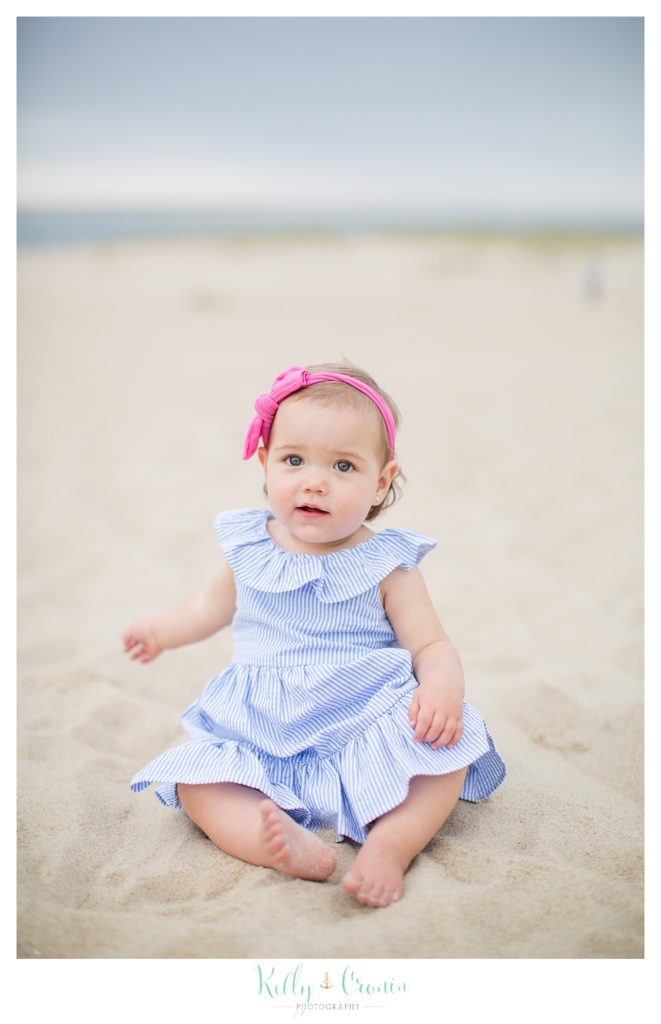 A baby girl sits in the sand. 