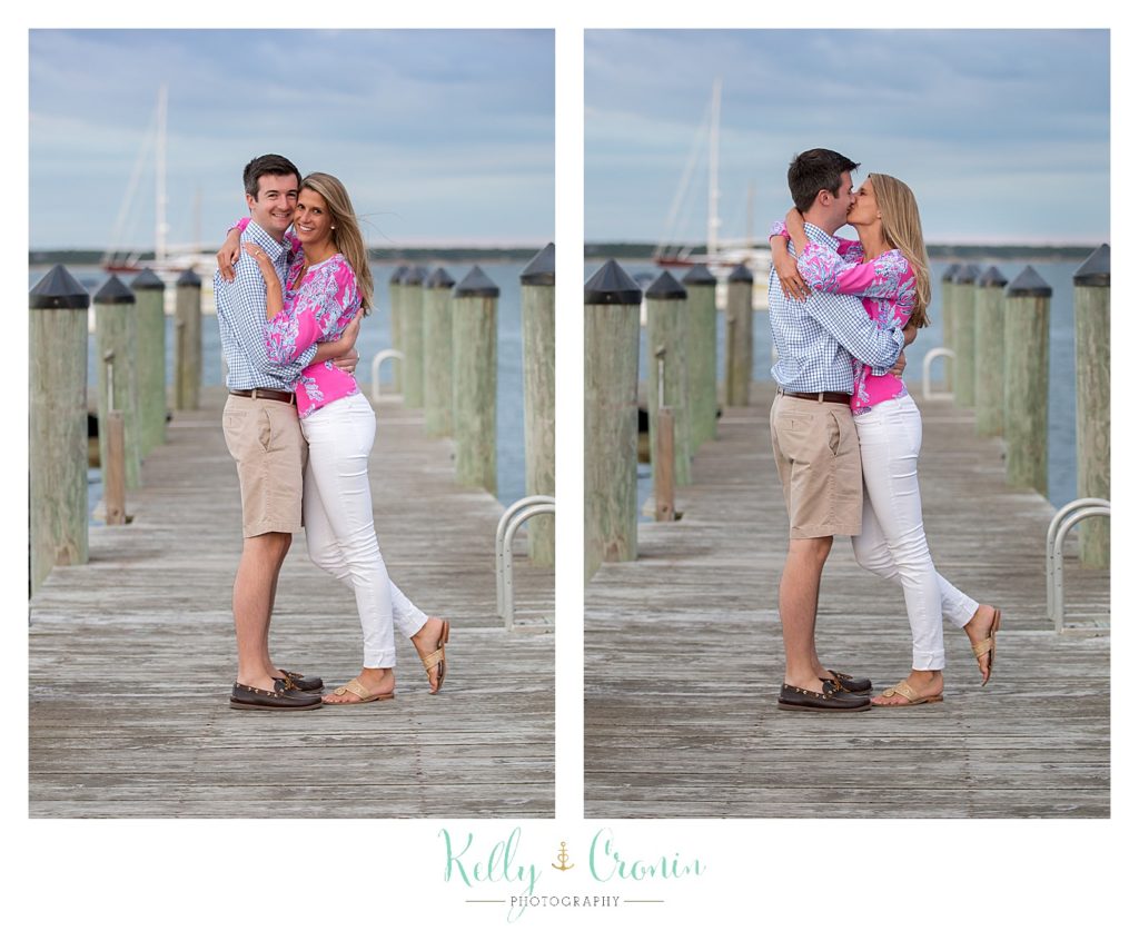 A couple hug each other while standing on a pier. 