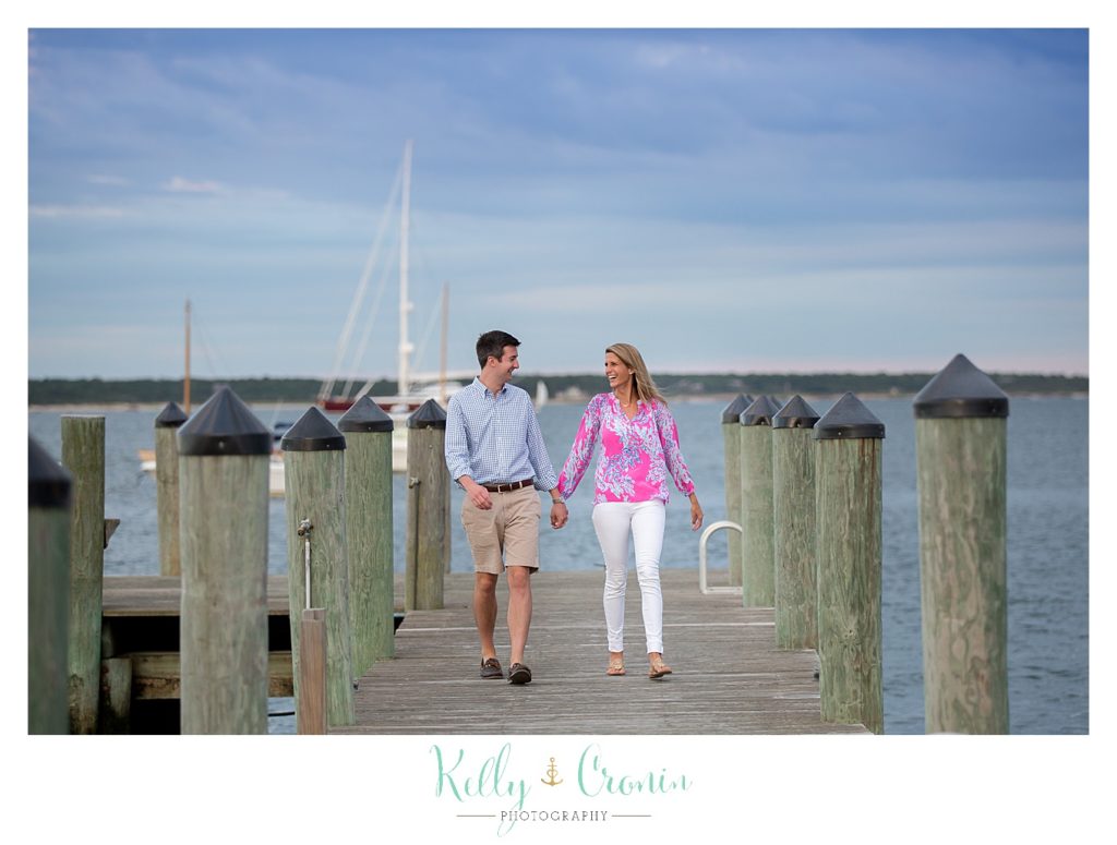 A couple hold hands and walk on a dock. 