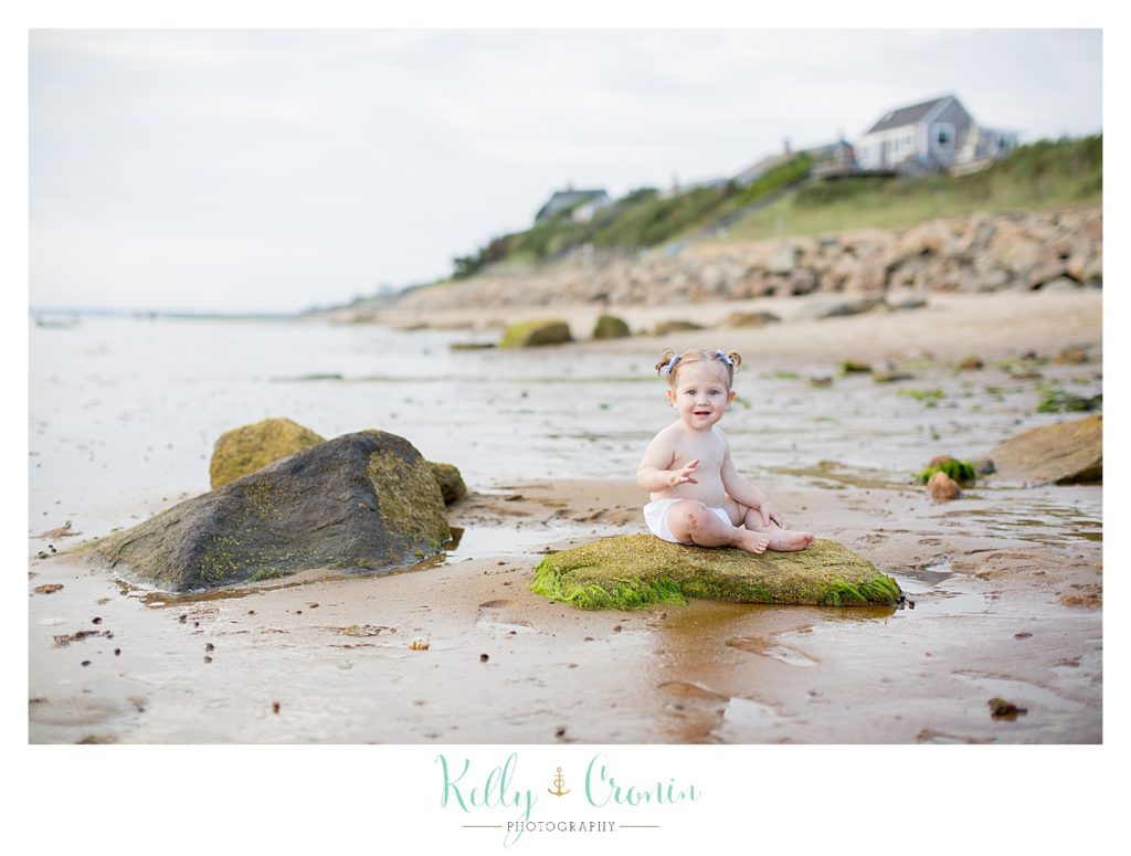 A baby sits in the water for her beach photos. 