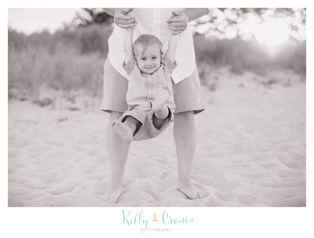 A father swings his baby between his legs. 