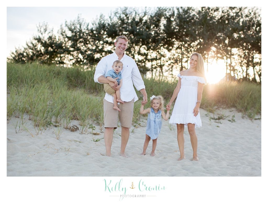 A family of four stands on the beach as the sun shines behind them. 