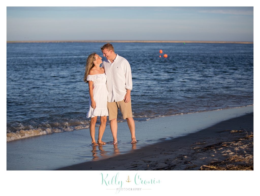 A man embraces his wife while standing in the water on the beach. 