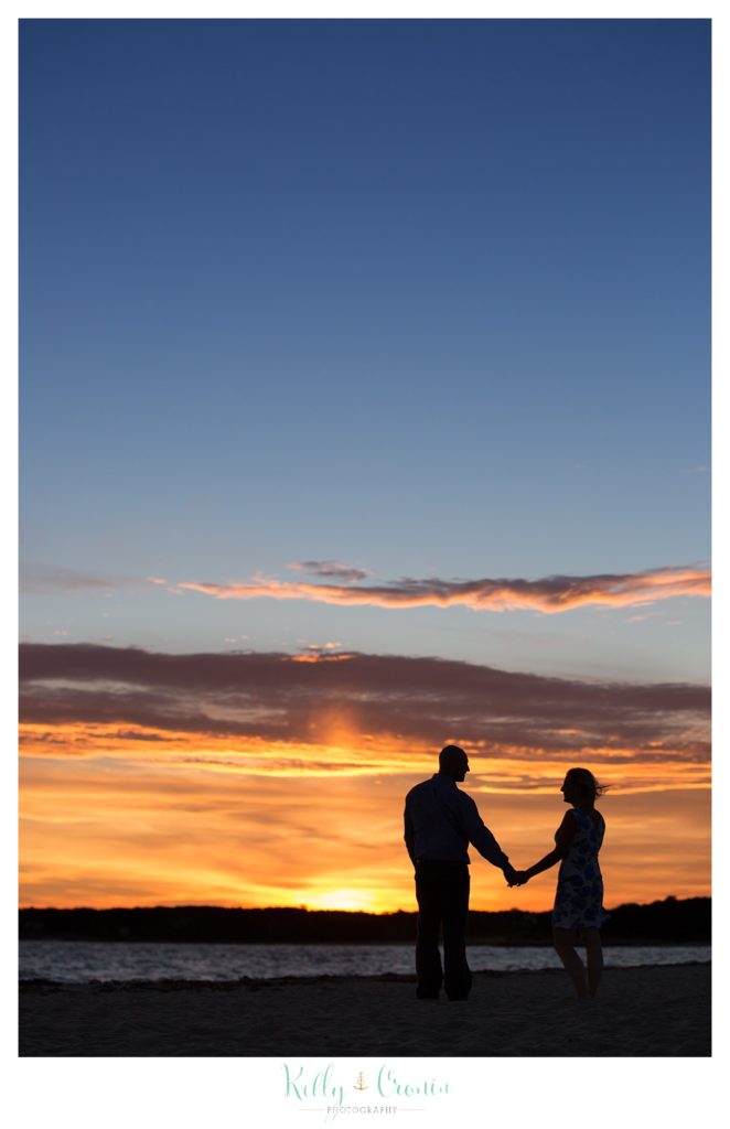 A couple hold hands in front of a sunset. 