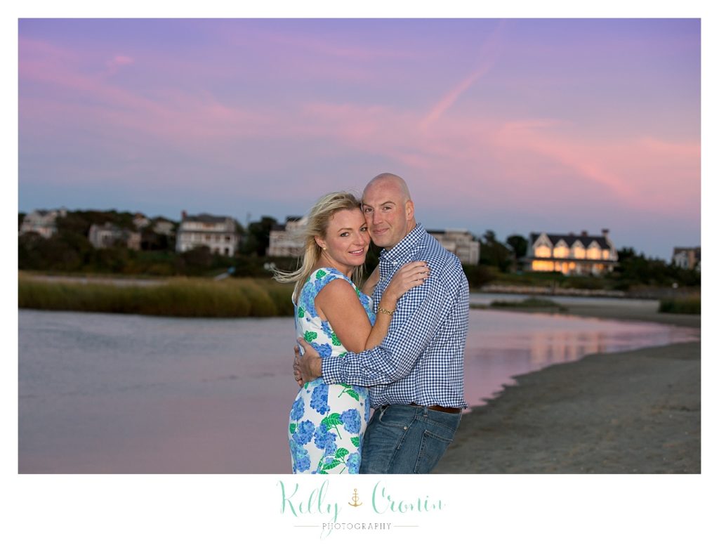 A couple embrace with a pink sunset around them. 