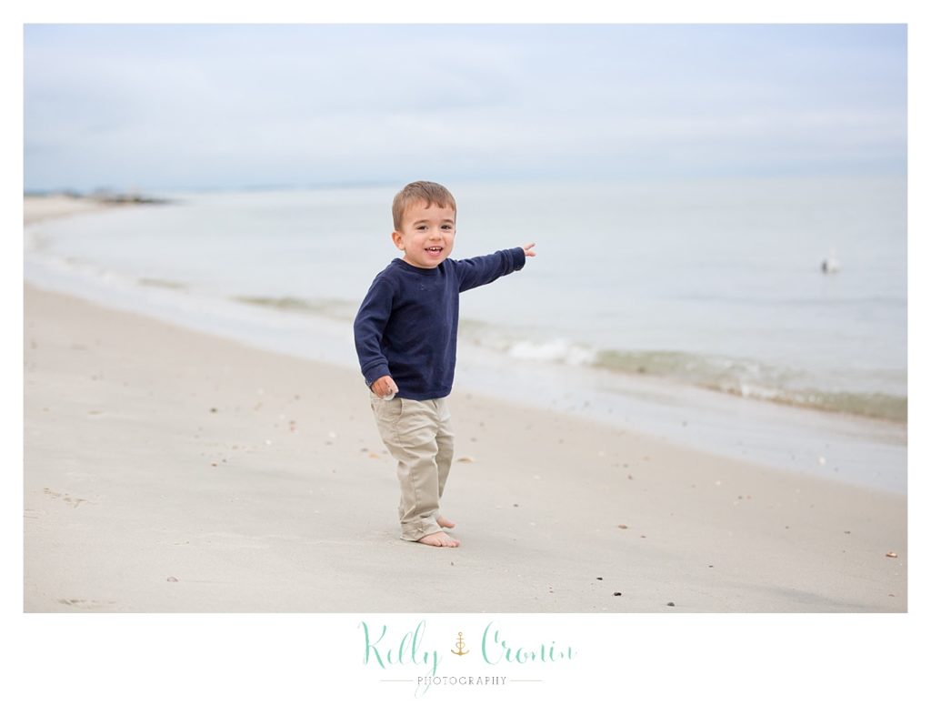 A toddler boy walks on the beach. 