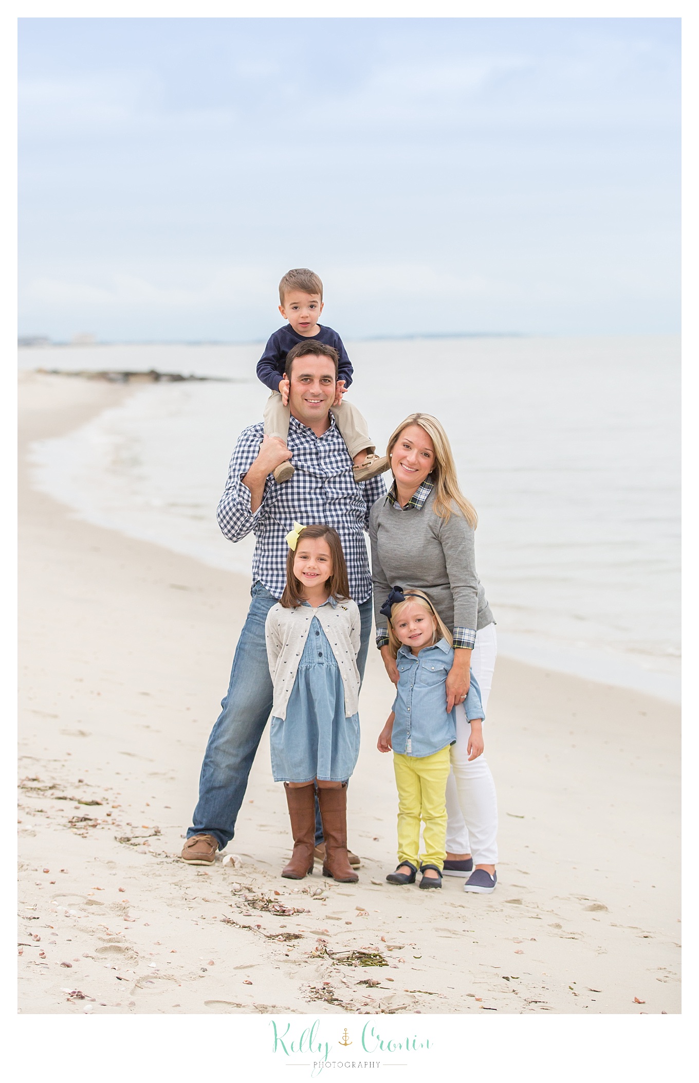 A family photographer captures a family standing on the beach.