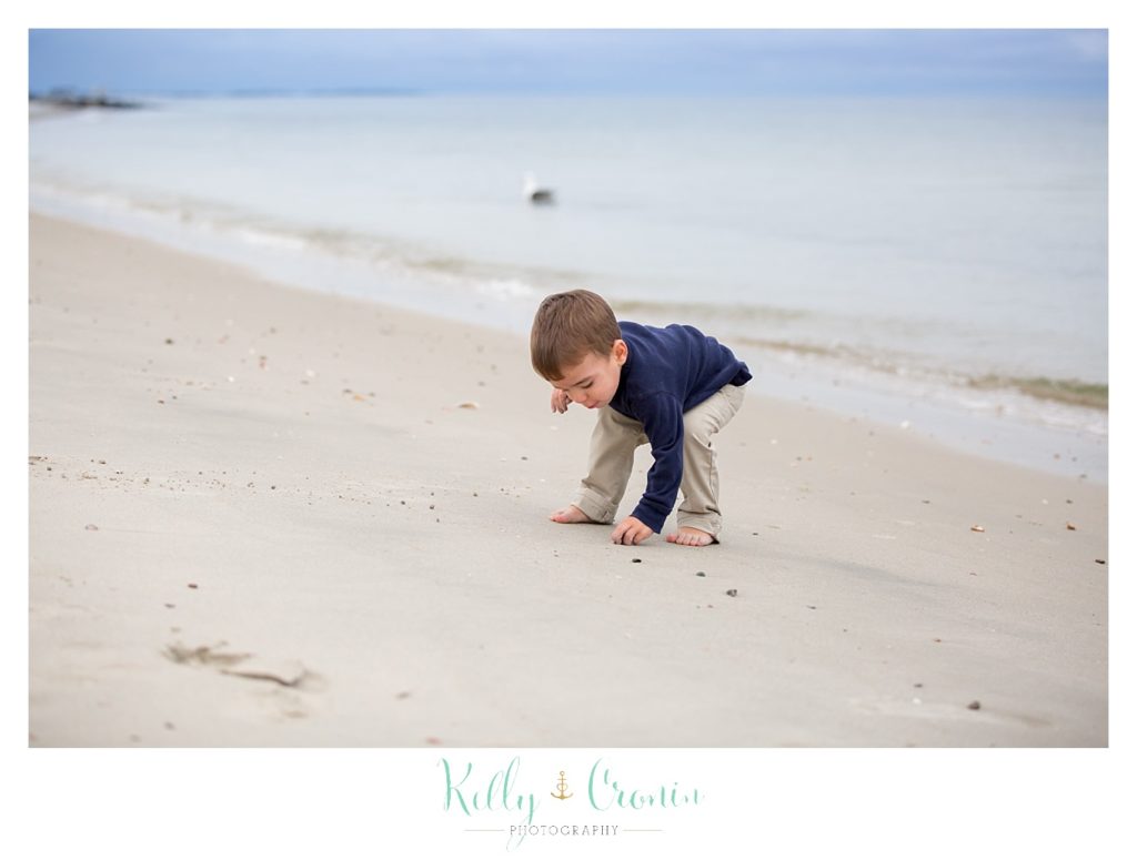 A boy bends down to inspect something on the beach. 