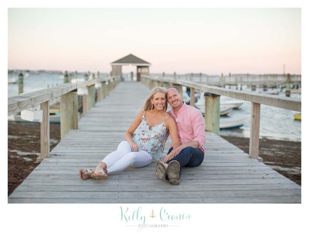 A couple sit on a pier for their Cape Cod Engagement Photos. 