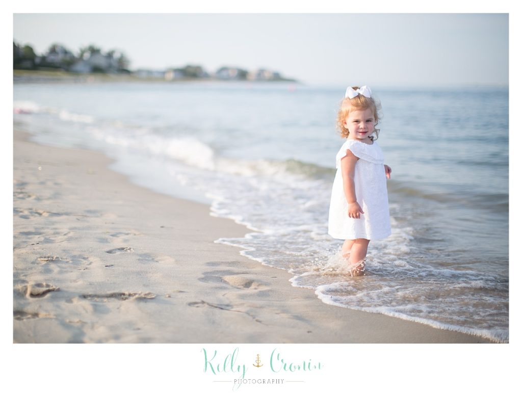A small girl walks into a wave on the beach. 
