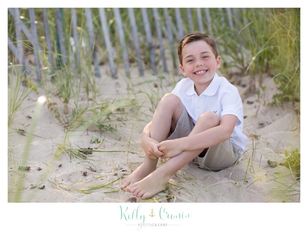 A boy sits in the sand holding his knees during his Cape Cod photography session. 