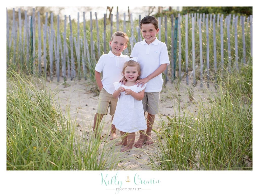 Three children crowd together while standing on the beach for their Cape Cod photography session. 