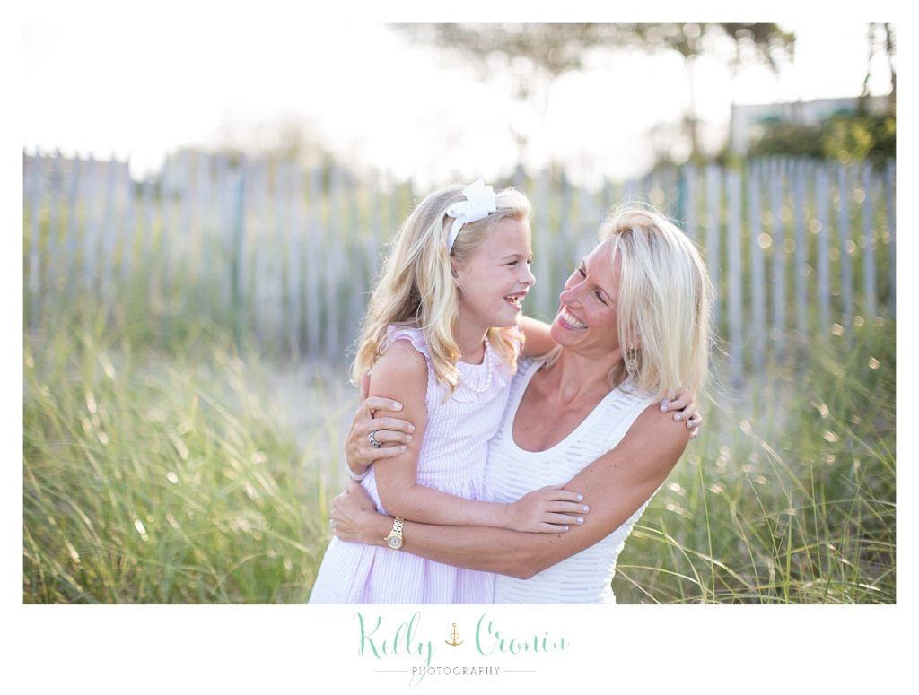 A mother and daughter wearing white dresses laugh together. 