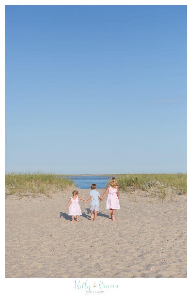 Three siblings take a walk on a sandy beach. 