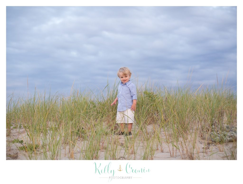 A boy is walking through the tall grass on the beach. 