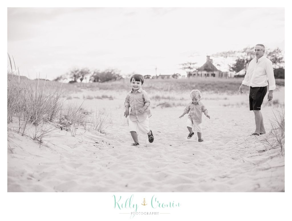 Two boys are running through the sandy beach together. 