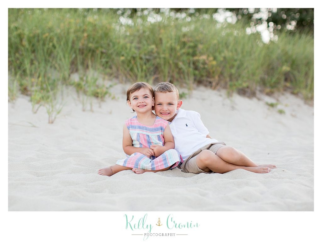 A boy hugs his sister as they sit on a beach together. 