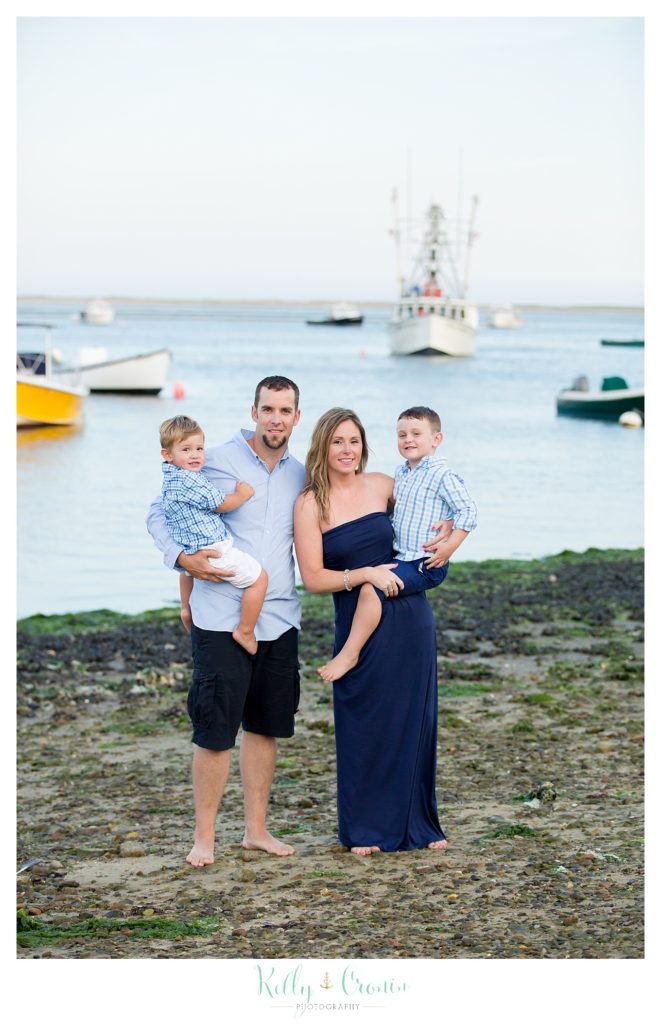 A family stands in front of boats on the water. 