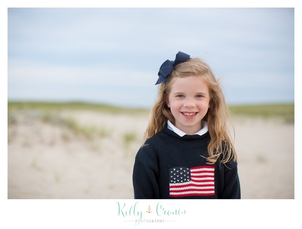 A girl wearing a flag sweater smiles. 